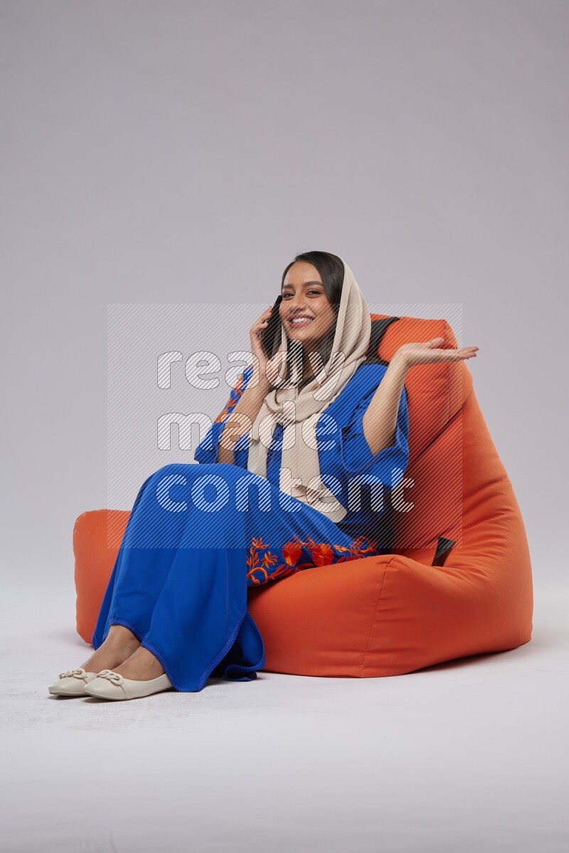 A Saudi woman wearing Jalabiya sitting on an orange beanbag and talking on the phone