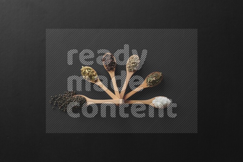 wooden spoons filled with white peppers, cloves, cardamom, salt, black peppers and basil on black flooring