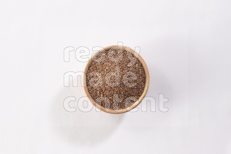 A wooden bowl full of flax seeds on a white flooring