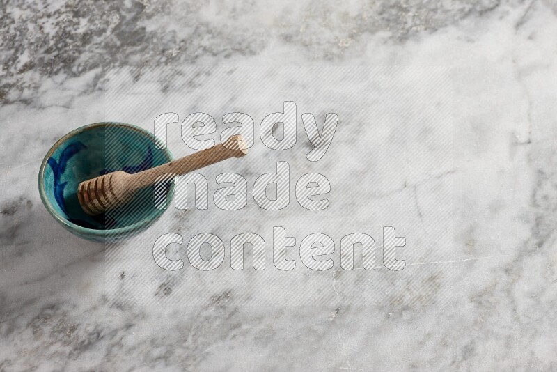 Decorative pottery bowl with wooden honey dipper in it on grey marble background