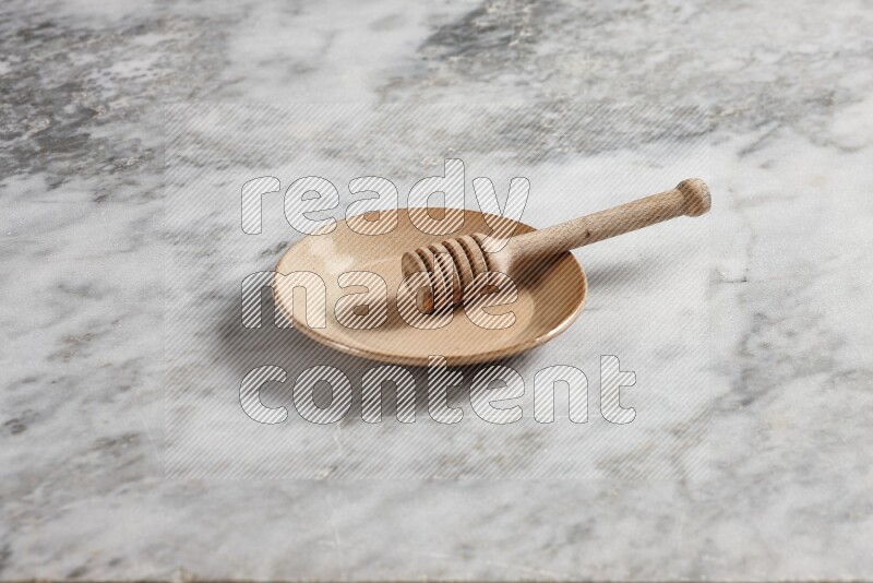 Beige pottery plate with wooden honey dipper in it on grey marble background