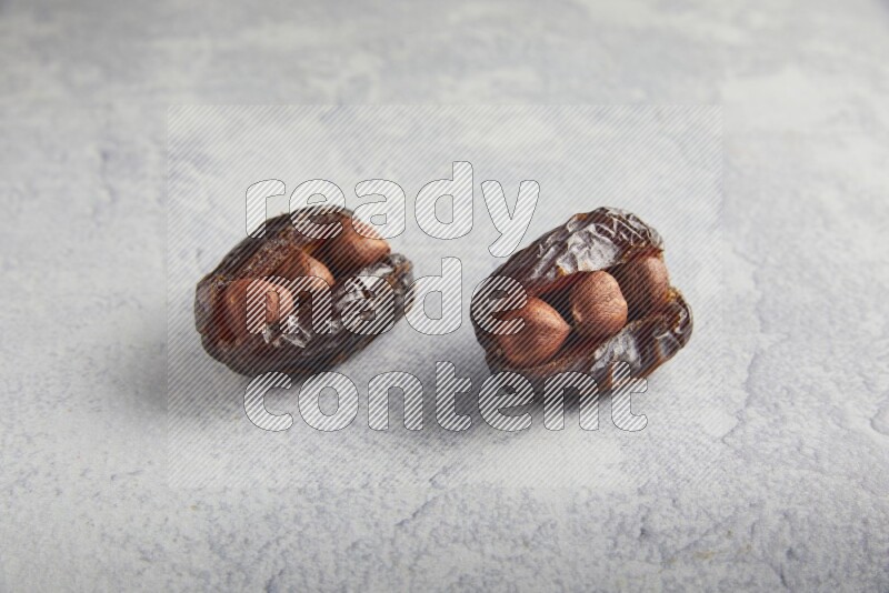 two hazelnuts stuffed madjoul dates on a light grey background