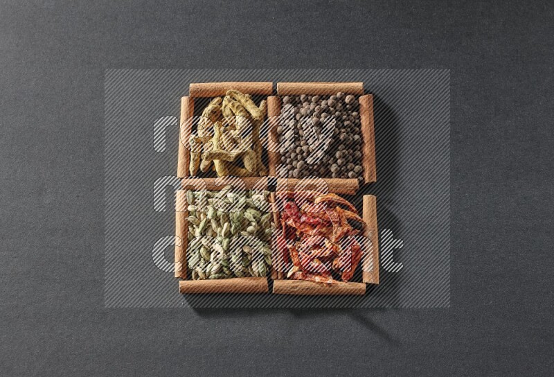 4 مربعات من عيدان القرفة ممتلئة بحبوب الهيل والفلفل الحار وبهار الفلفل الحلو وأصابع الكركم على أرضية سوداء