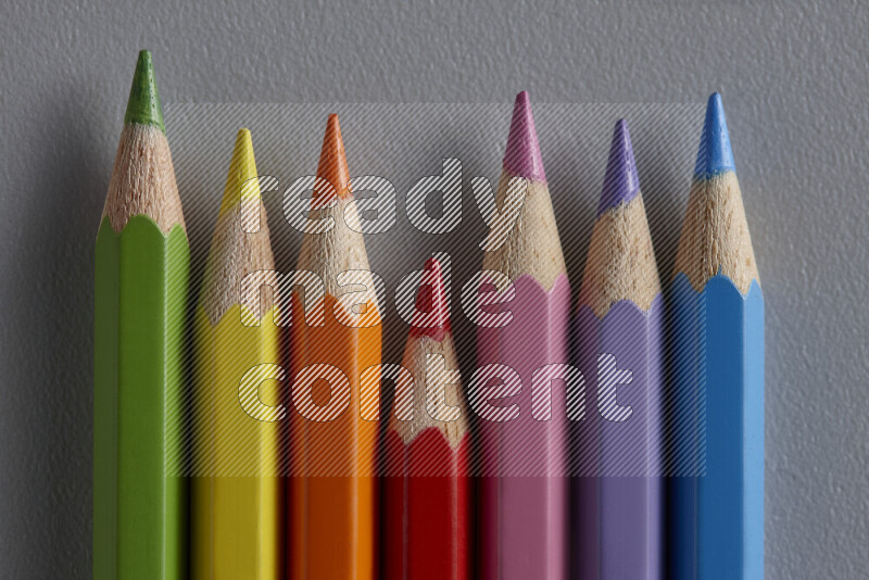 A collection of colored pencils arranged showcasing a gradient of different hues on grey background