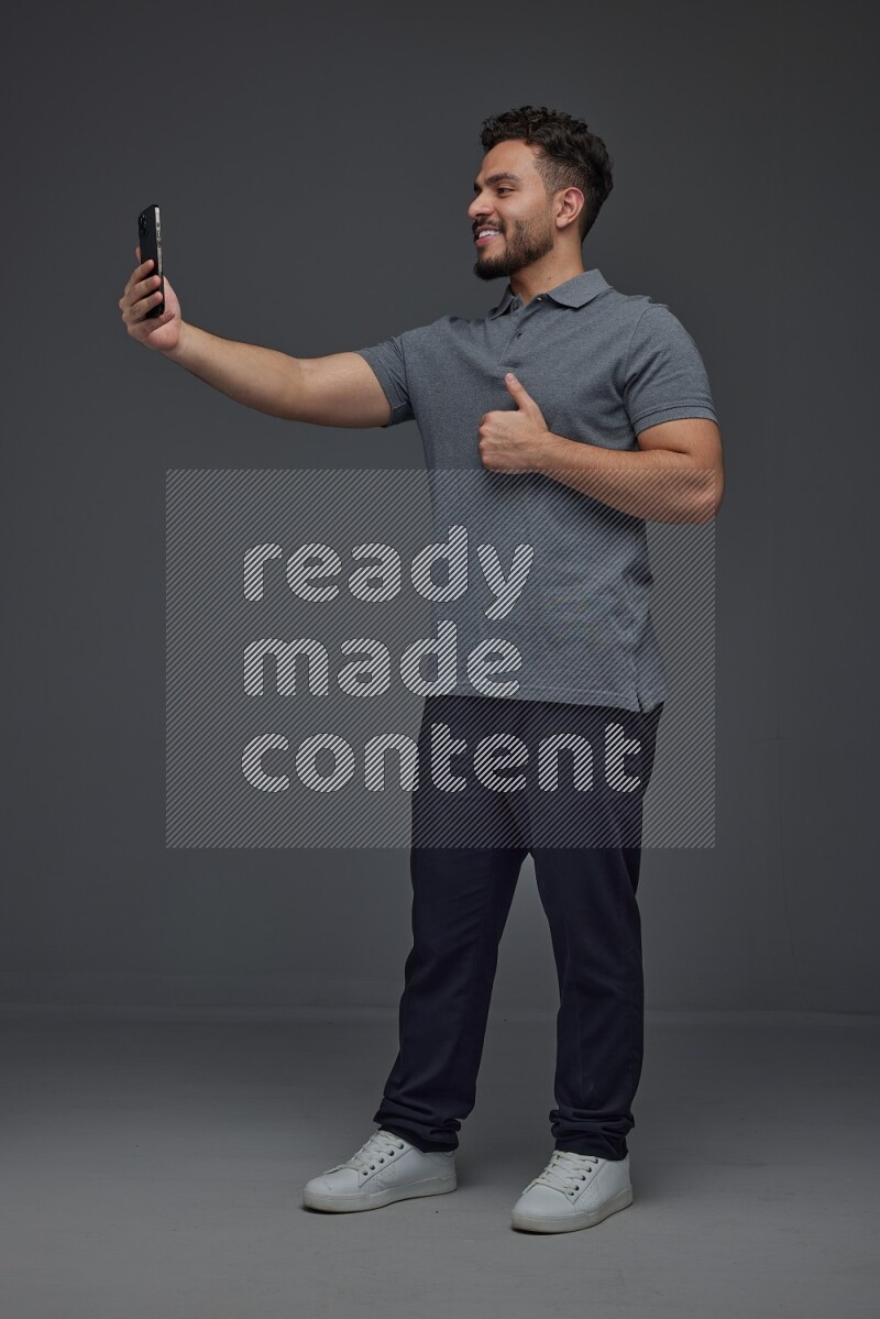A man wearing casual and taking selfie with his phone different angles eye level on a gray background