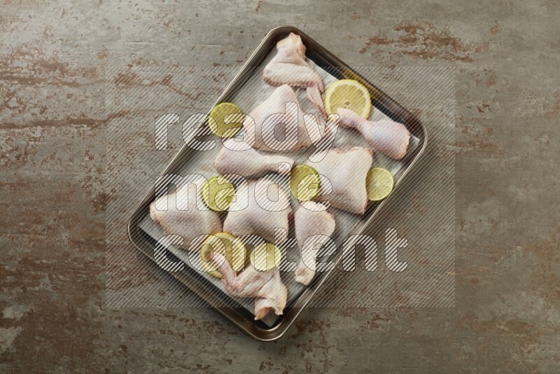 Mixed fresh chicken pieces in an oven tray on a textured rustic background