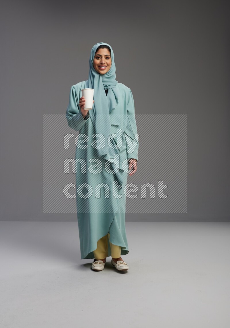 Saudi Woman wearing Abaya standing  holding paper cup on Gray background