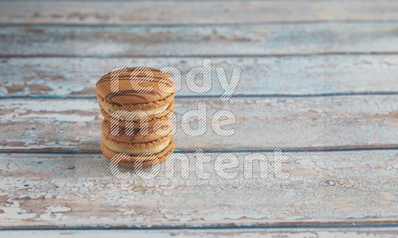 45º Shot of two light brown Almond Cream macarons on light blue wooden background