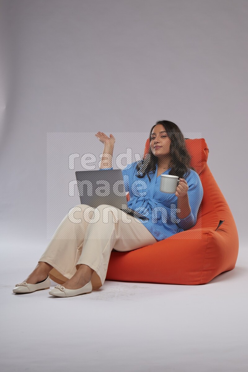 A woman sitting on an orange beanbag and working on laptop