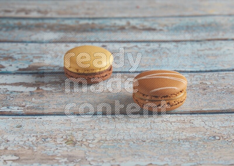 45º Shot of of two assorted Brown Irish Cream, and Yellow, and Brown Chai Latte macarons  on light blue background