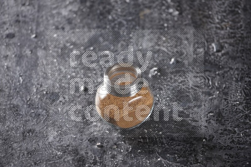 Herbal glass jar full of cinnamon powder on a textured black background
