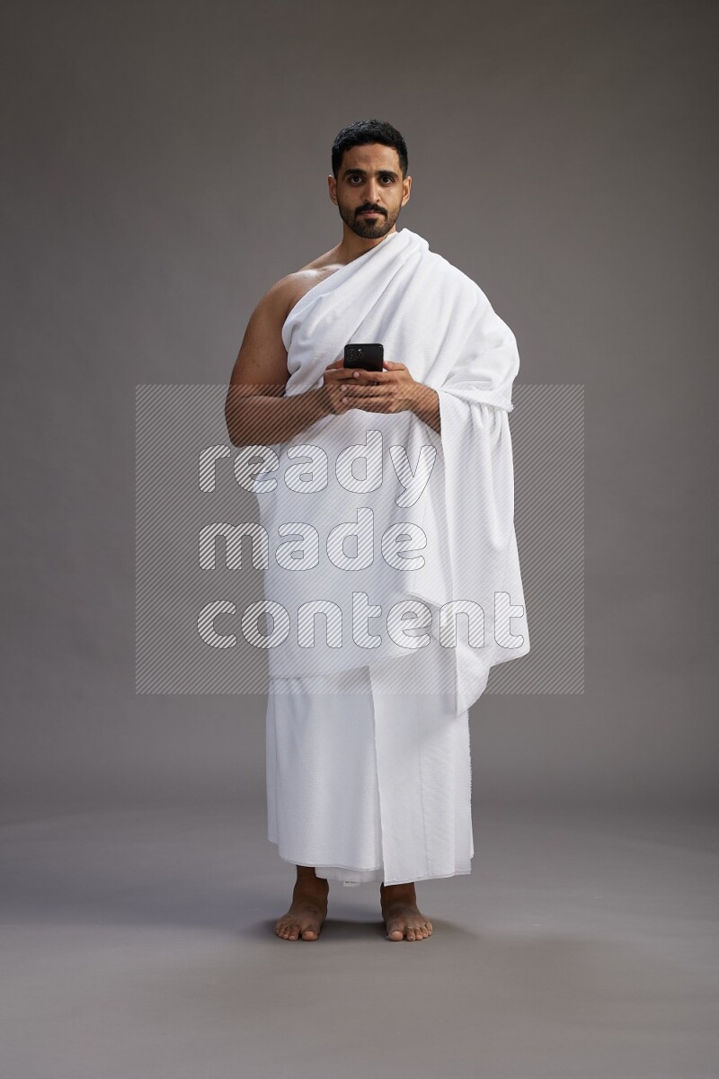 A man wearing Ehram Standing texting on phone on gray background