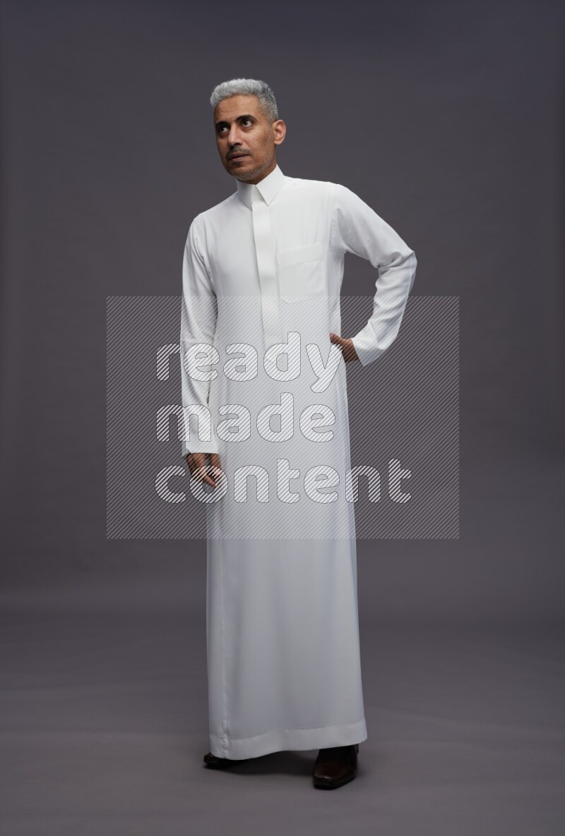Saudi man wearing thob standing interacting with the camera on gray background