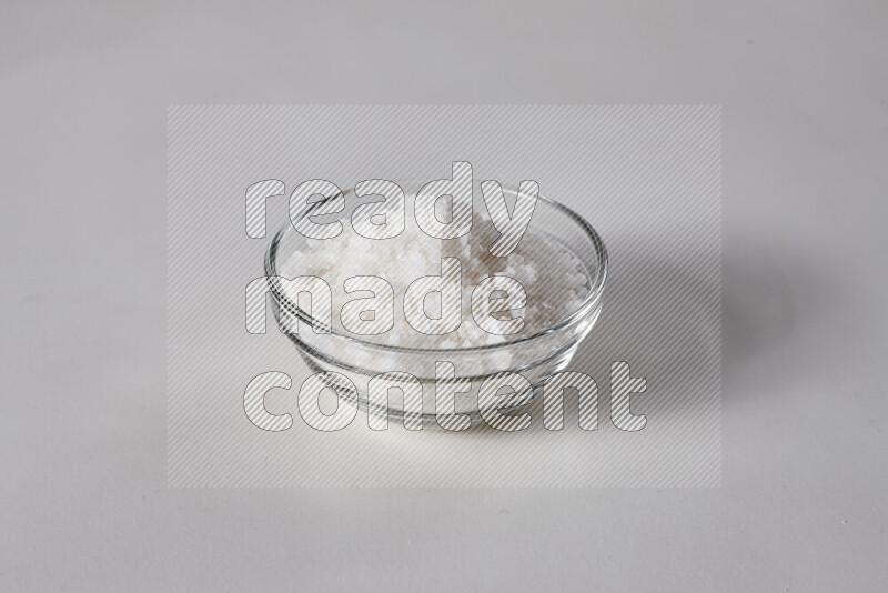 A glass bowl full of coarse sea salt crystals on white background