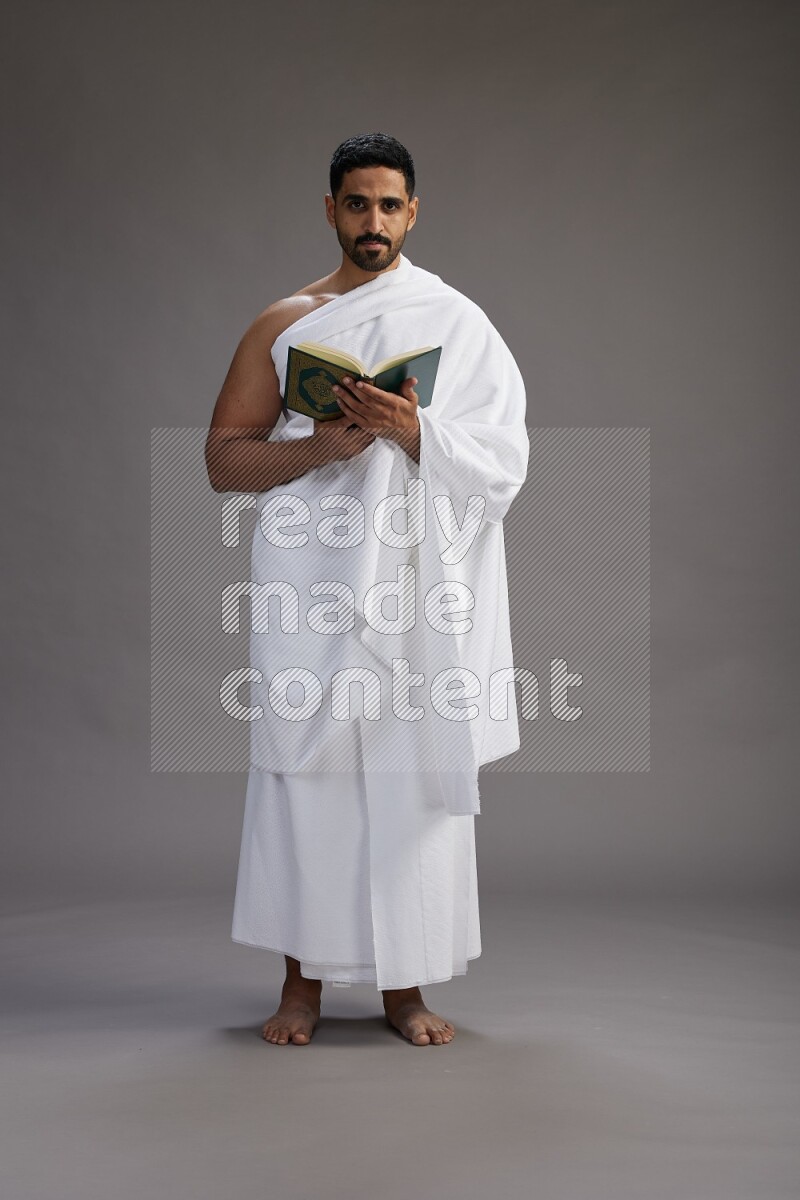 A man wearing Ehram Standing reading quran on gray background