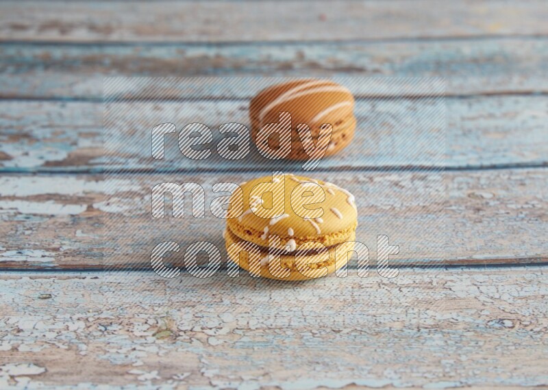 45º Shot of of two assorted Brown Irish Cream, and Yellow Piña Colada macarons on light blue background