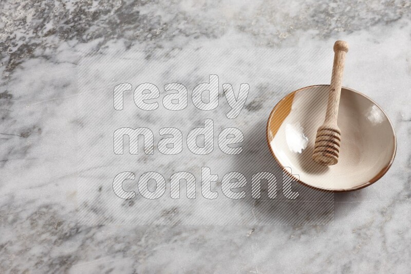 Multicolored pottery plate with wooden honey dipper in it on grey marble background