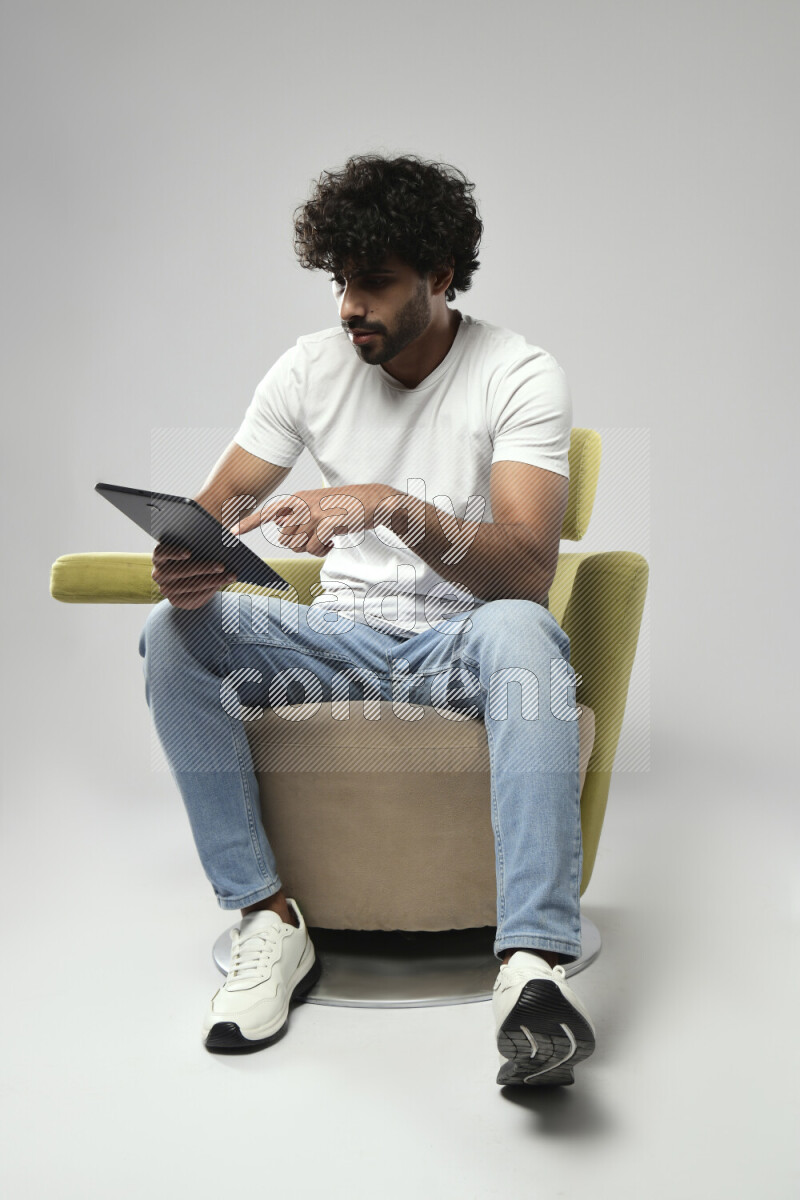 A man wearing casual sitting on a chair browsing on a tablet on white background