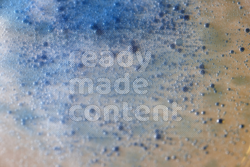 Close-ups of abstract blue watercolor drops on oil Surface on yellow background