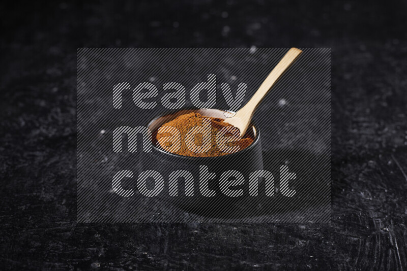 A black pottery bowl full of ground paprika powder on black background
