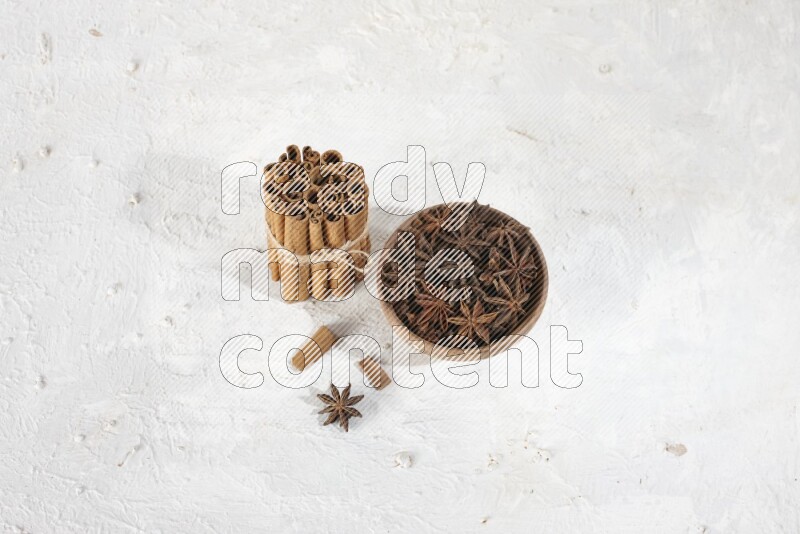 A stacked and bounded cinnamon sticks and a wooden bowl full of star anise on a white background