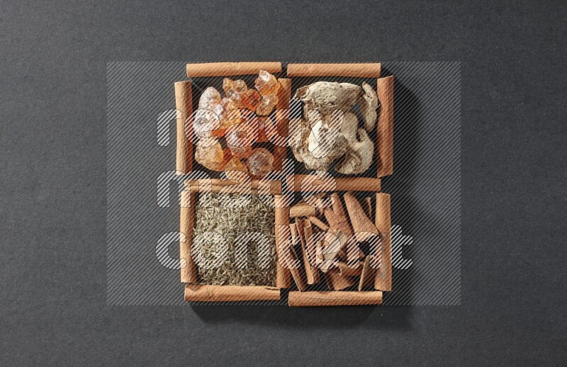 4 squares of cinnamon sticks full of gum arabic, dried ginger, cinnamon and cumin on black flooring