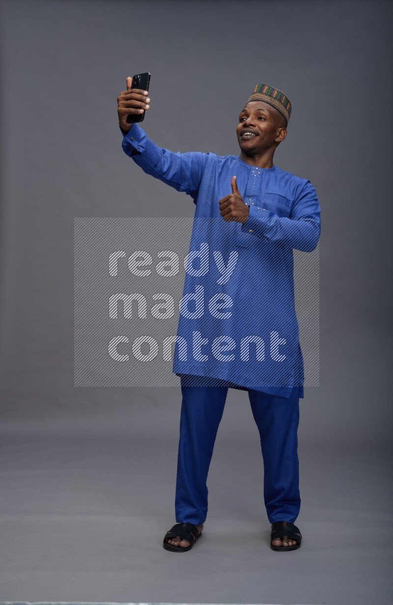Man wearing Nigerian outfit standing taking selfie on gray background