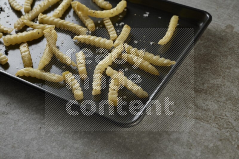 crinkle fries in a black stainless steel rectangle tray on grey textured counter top