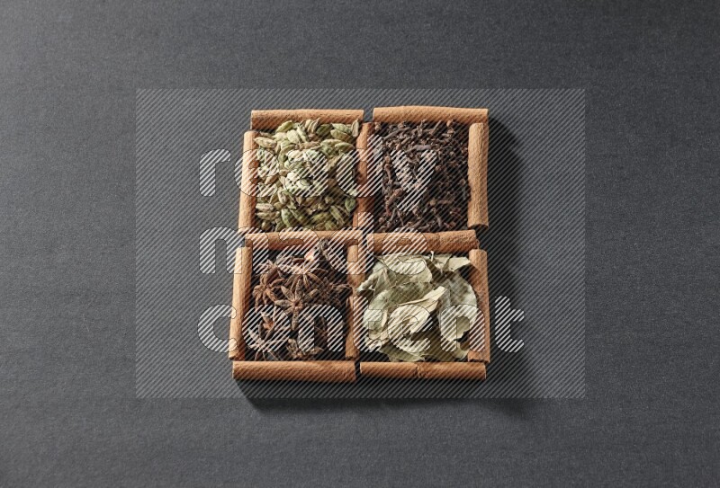 4 squares of cinnamon sticks full of star anise, cardamom, cloves and bay laurel leaves on black flooring