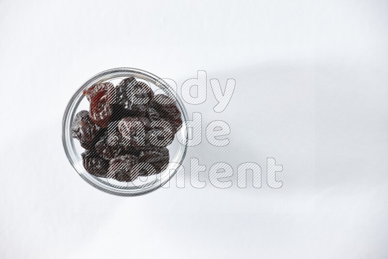A glass bowl full of dried plums on a white background in different angles