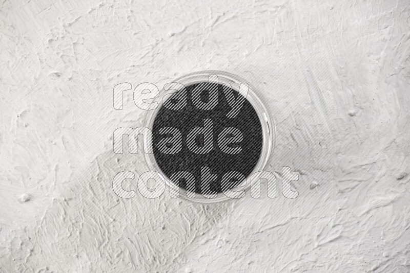 A glass jar full of black seeds on a textured white flooring