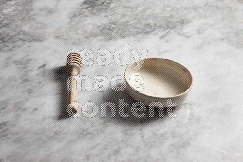 Beige pottery bowl with wooden honey dipper on the side on grey marble background