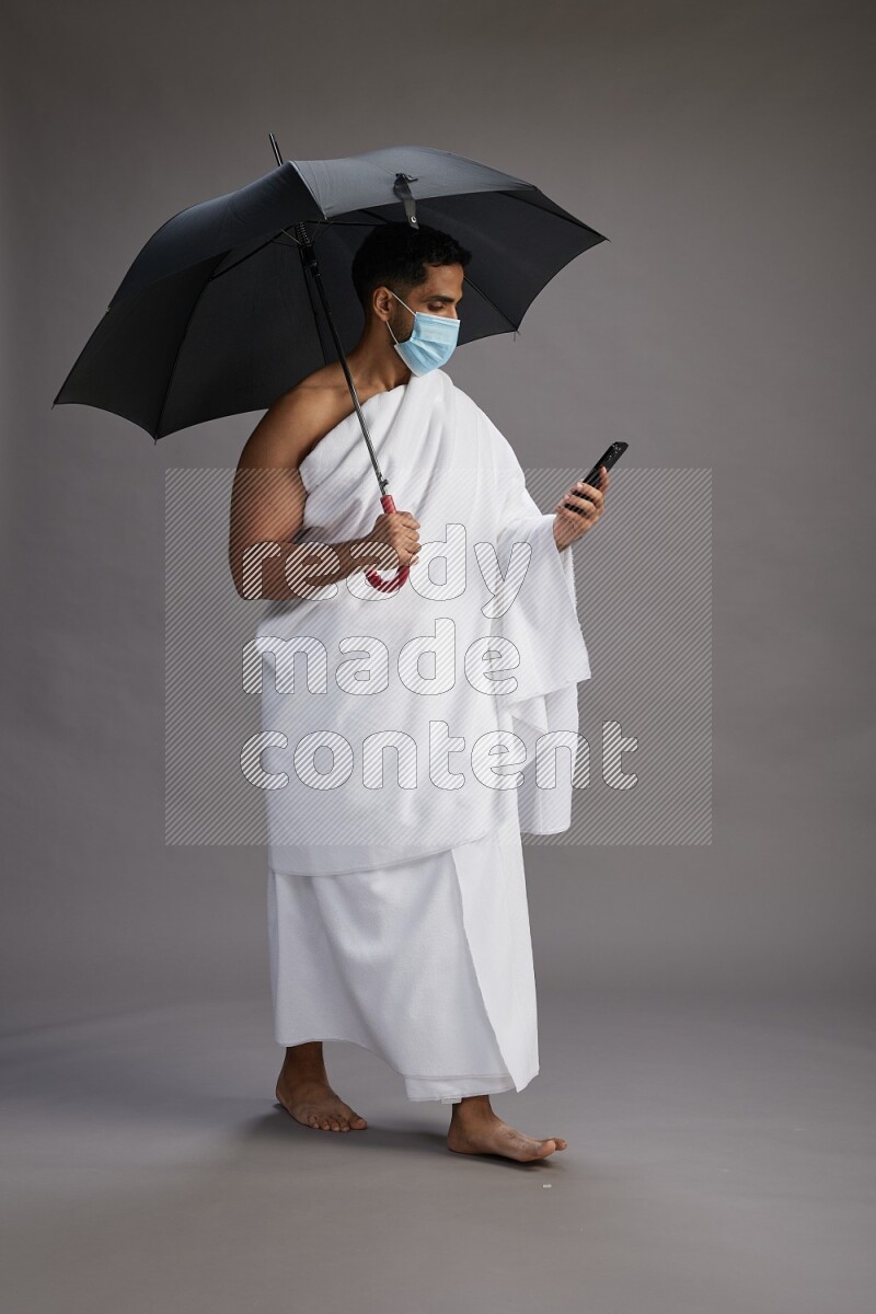 A man wearing Ehram and mask Standing holding umbrella on gray background on gray background