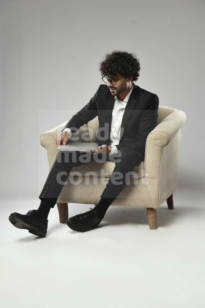 A man wearing formal sitting on a chair holding a laptop on white background