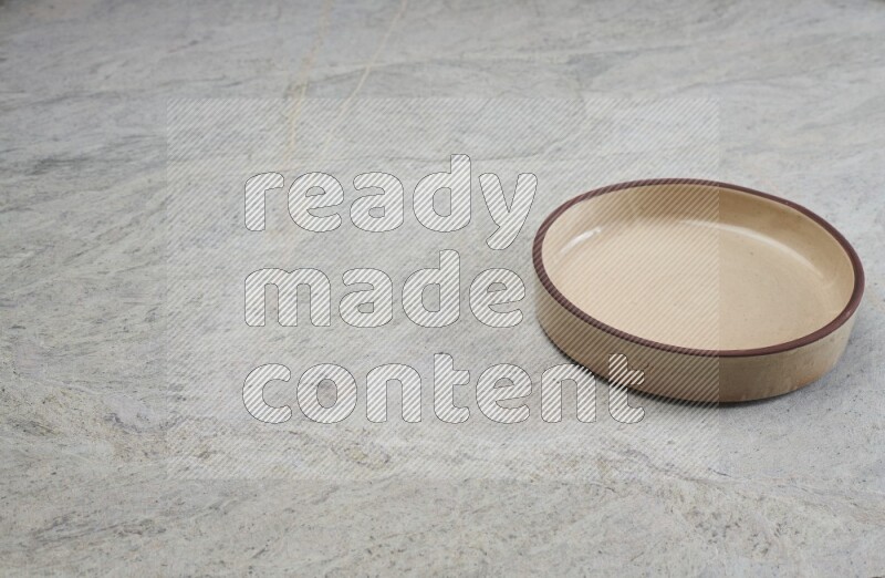 A beige pottery oven bowl on grey marble background