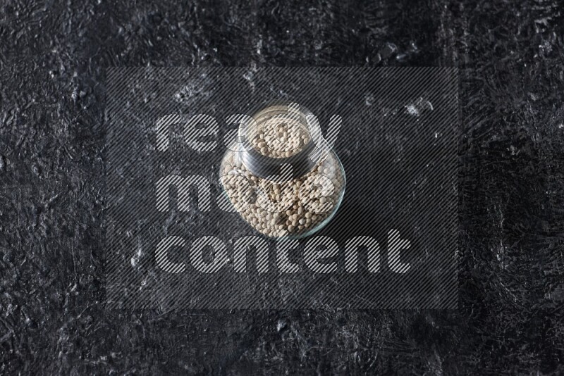 Herbal glass jar full of white pepper on textured black flooring