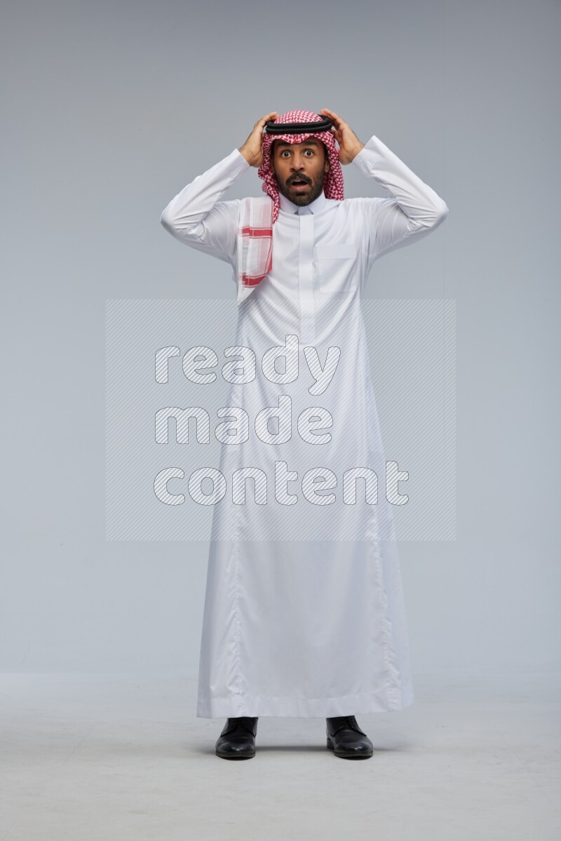 Saudi man Wearing Thob and shomag standing interacting with the camera on Gray background
