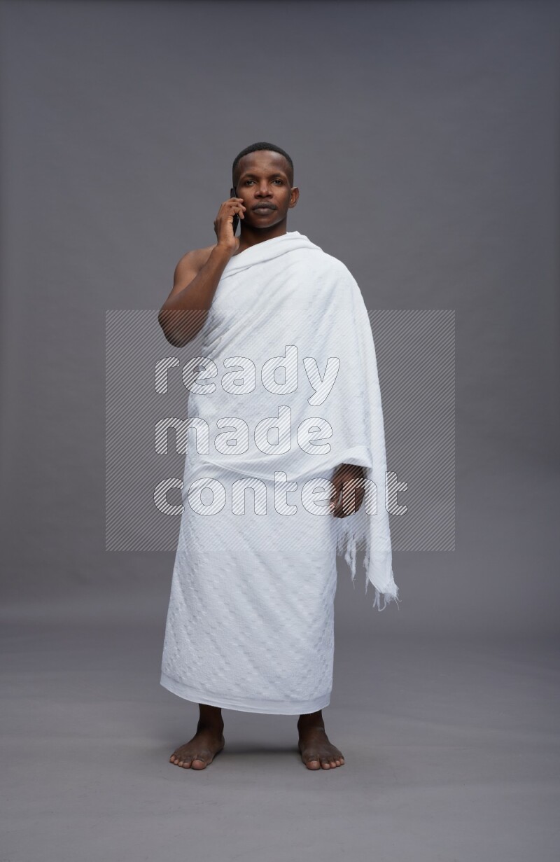 A man wearing Ehram Standing talking on phone on gray background