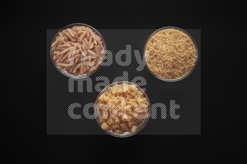 Different pasta types in glass bowls on black background