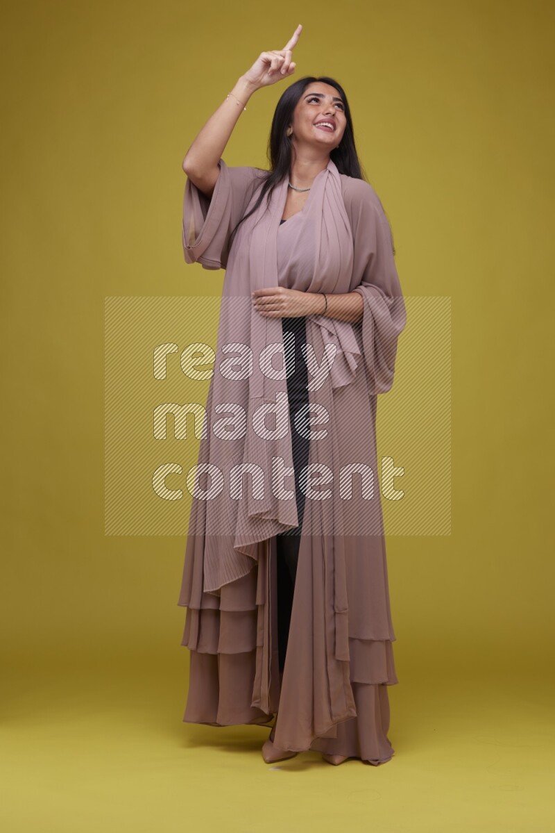A woman Pointing on a Yellow Background wearing Brown Abaya