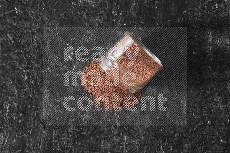A glass jar full of garden cress seeds flipped and seeds spread out on a textured black flooring