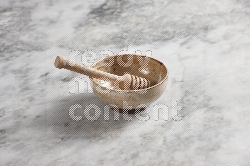 Beige pottery bowl with wooden honey dipper in it on grey marble background