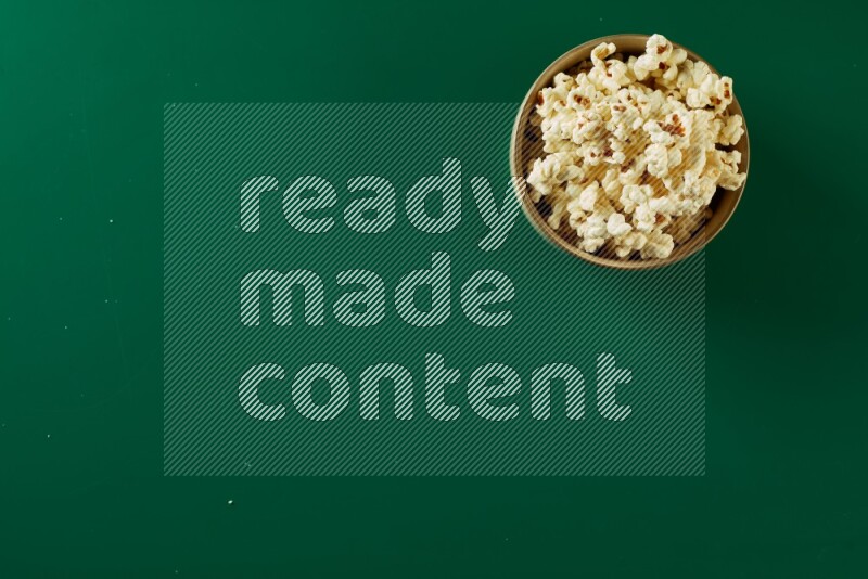 An off white ceramic bowl full of popcorn on a green background in a top view shot