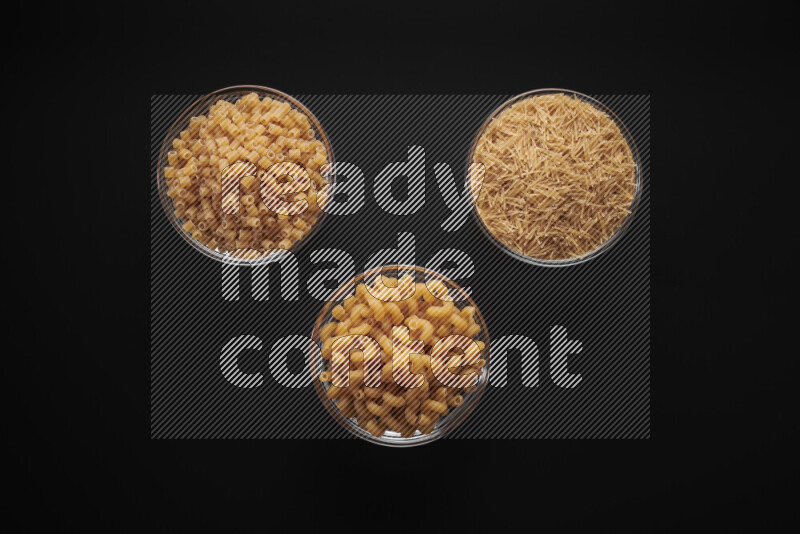 Different pasta types in glass bowls on black background