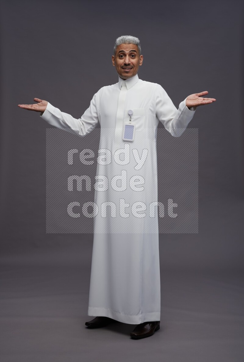 Saudi man wearing thob with pocket employee badge standing interacting with the camera on gray background