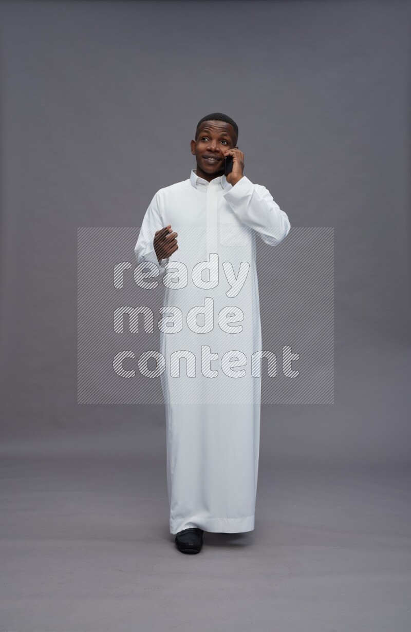 Saudi man wearing thob standing talking on phone on gray background