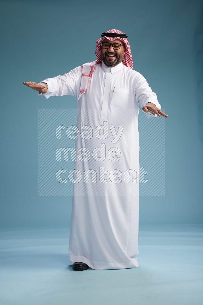 Saudi Man with shimag Standing Interacting with the camera on blue background