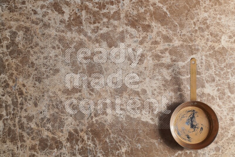 A small copper pan on beige marble background