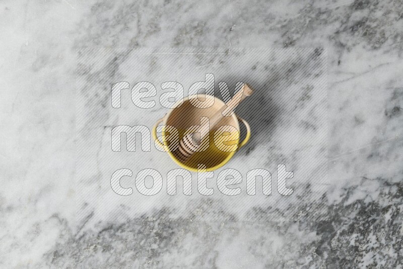 Multicolored pottery bowl with wooden honey dipper in it on grey marble background