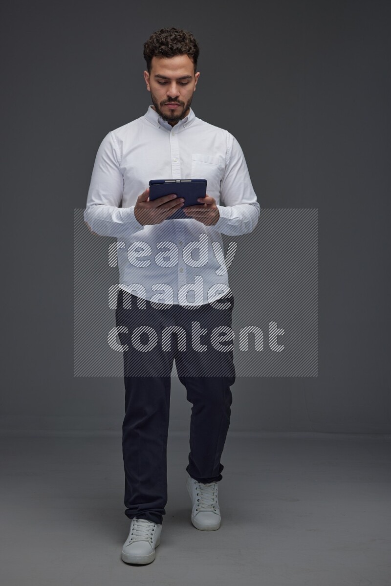 A man wearing smart casual standing and using his tablet eye level on a gray background